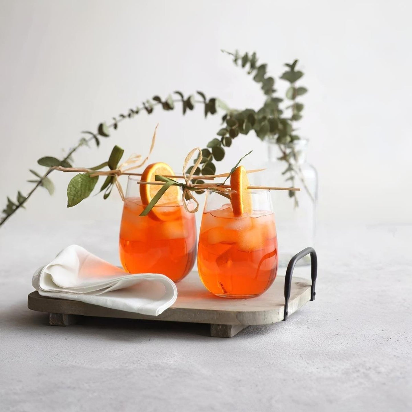 Two orange cocktails with garnishes on a wooden tray with a light background